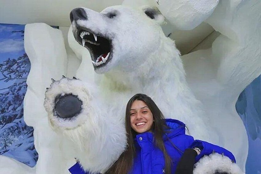 A person in a blue jacket posing with a large polar bear statue. 2