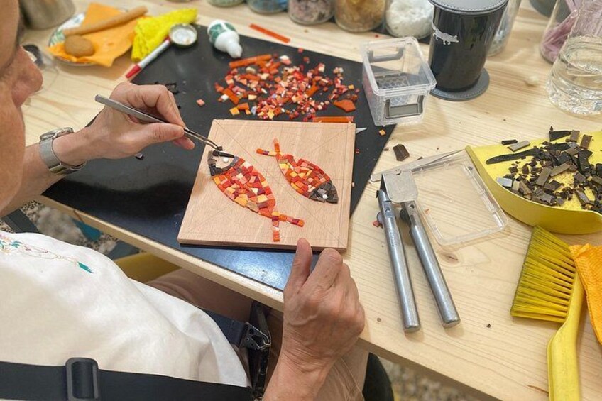 A person working on a wooden board with colorful materials, using tools like a brush and a metal object. 1