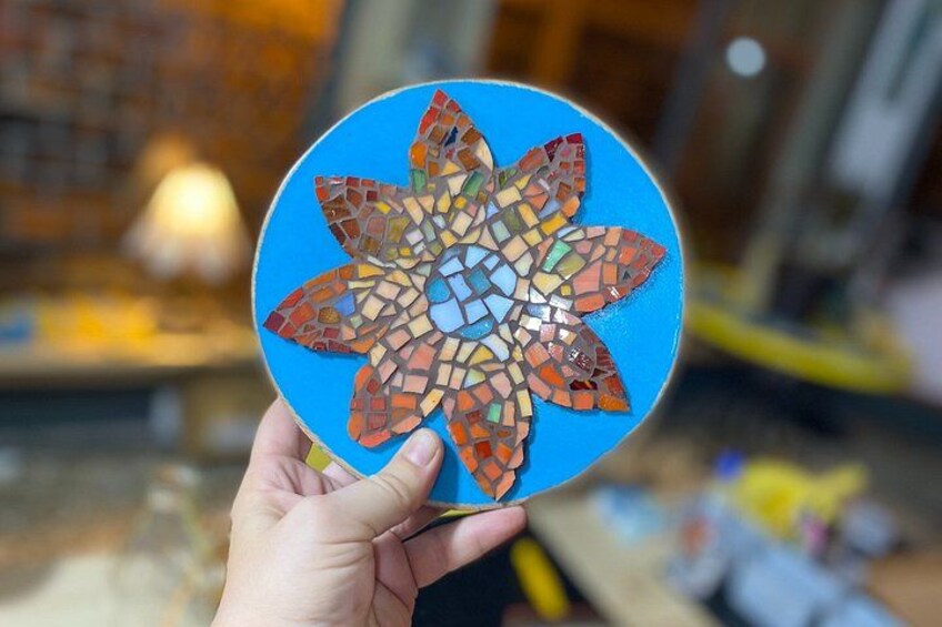 A hand holding a round mosaic tile with a blue background and a multicolored floral pattern. 3