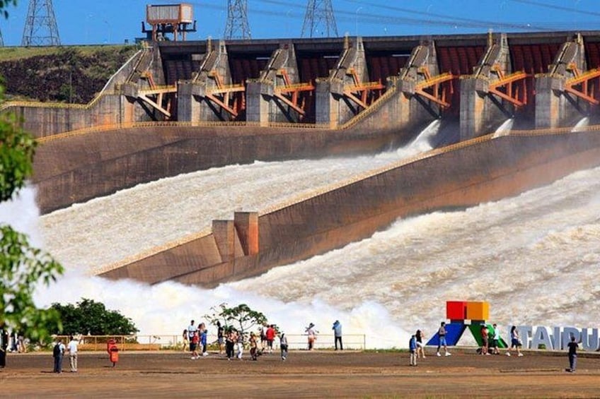 A dam with water flowing over spillways, a playground with colorful equipment, and a clear sky. 4