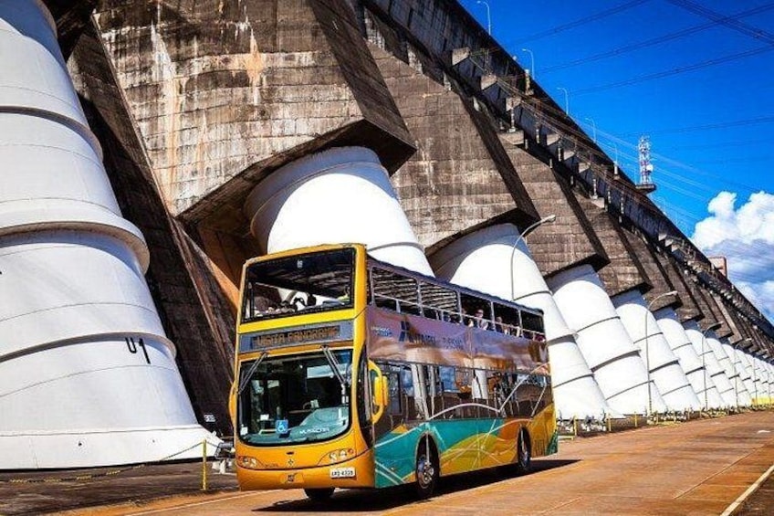 A double-decker bus parked under a large concrete bridge with cylindrical structures. 2