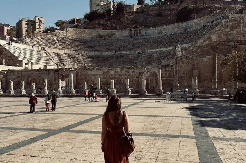 An ancient amphitheater with stone seating and columns, surrounded by a paved plaza. 4