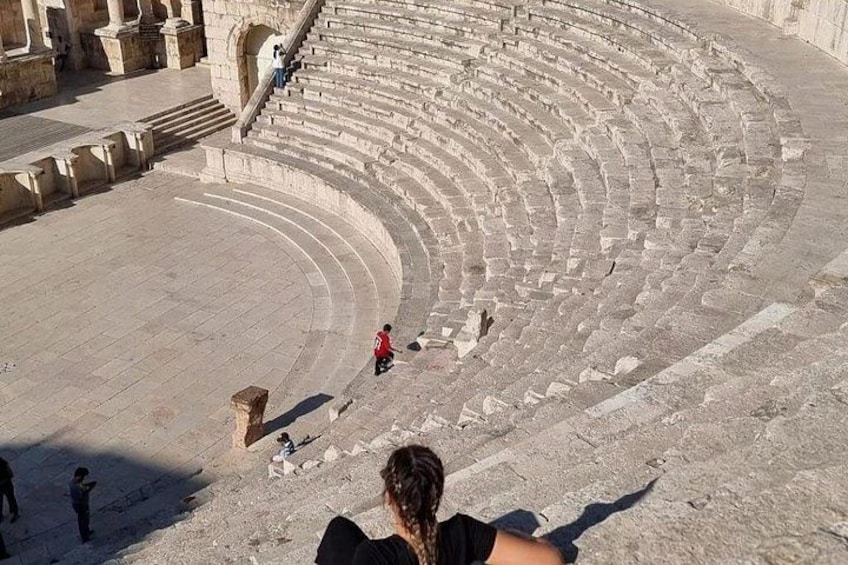 An ancient amphitheater with stone steps and a few people. 2