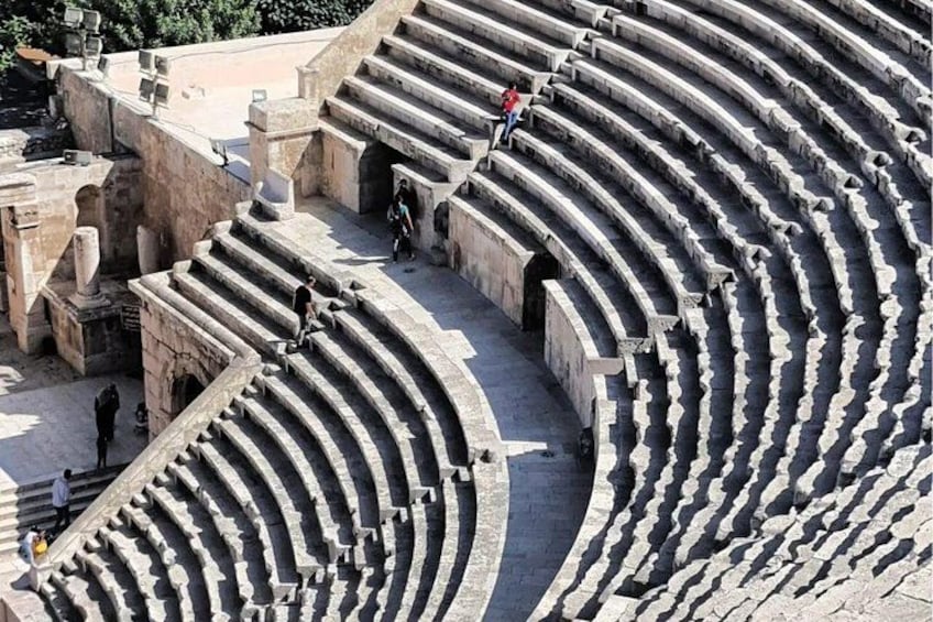 An ancient amphitheater with tiered stone seating and a few people walking around. 5