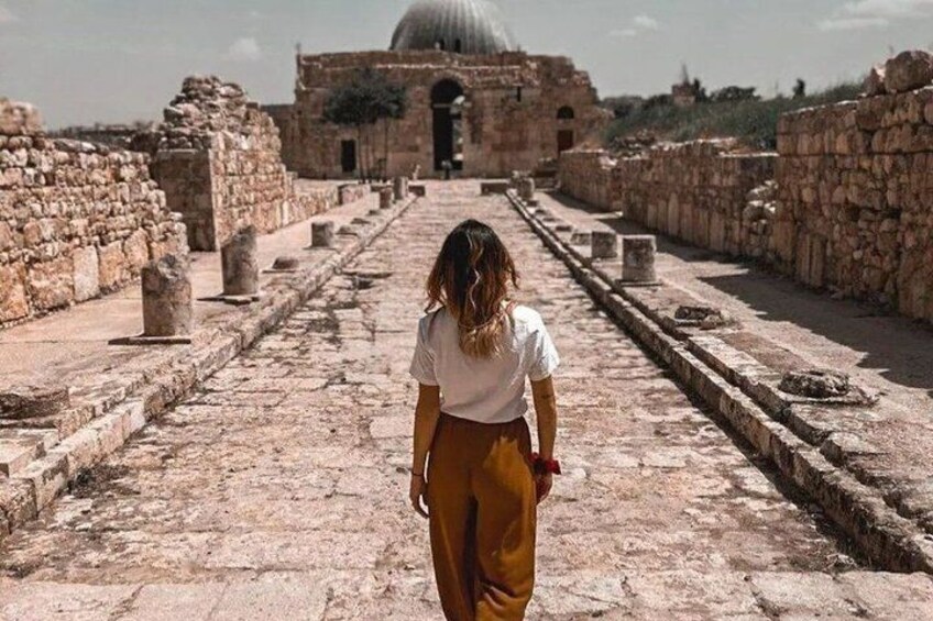A person walking on an ancient stone pathway with ruins on either side and a large dome structure in the background. 3