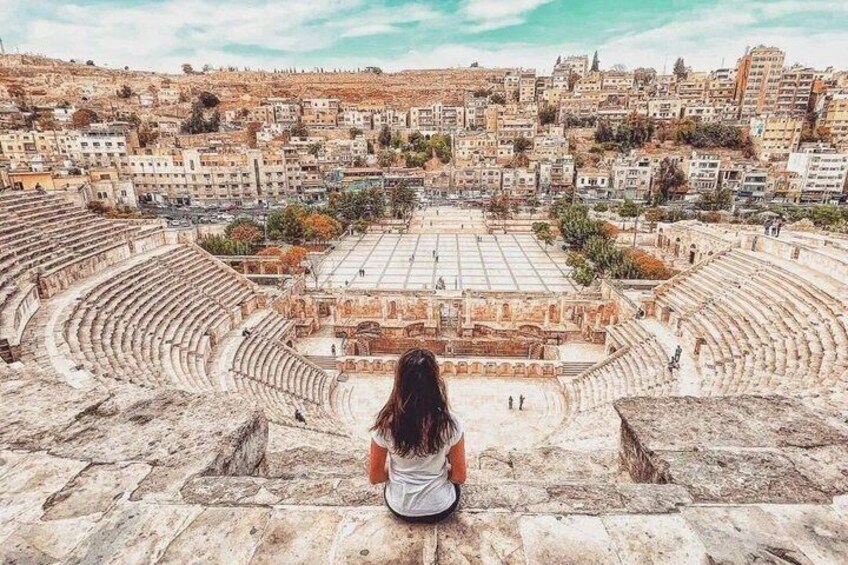 An ancient amphitheater with a person sitting in the foreground. 2