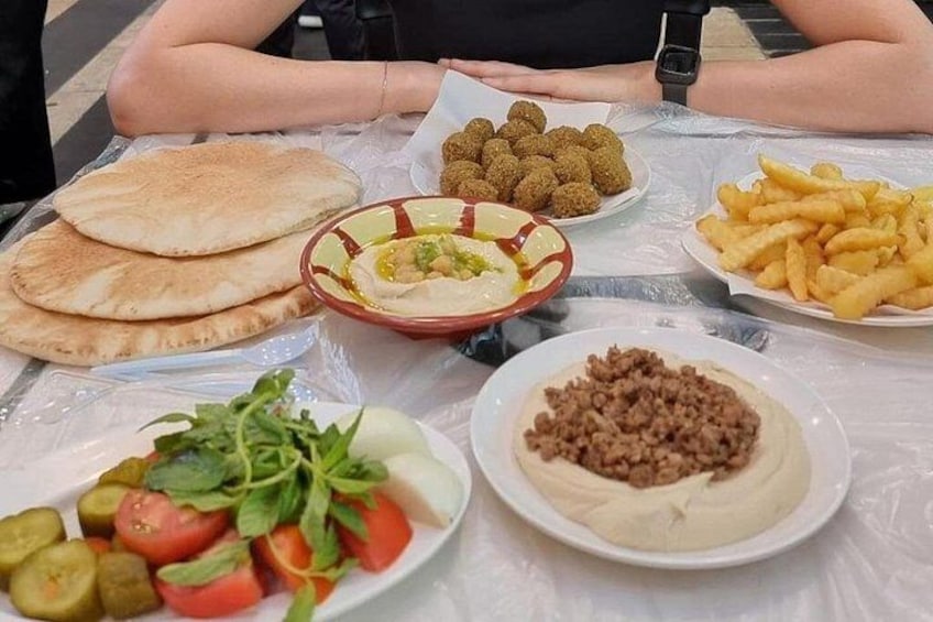 A table with various food items including flatbreads, hummus, fries, and a salad. 1