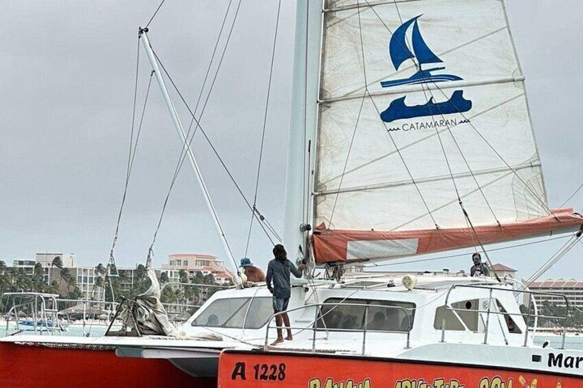 A sailboat with a logo on its sail, a person standing on the deck, and a cityscape in the background. 2