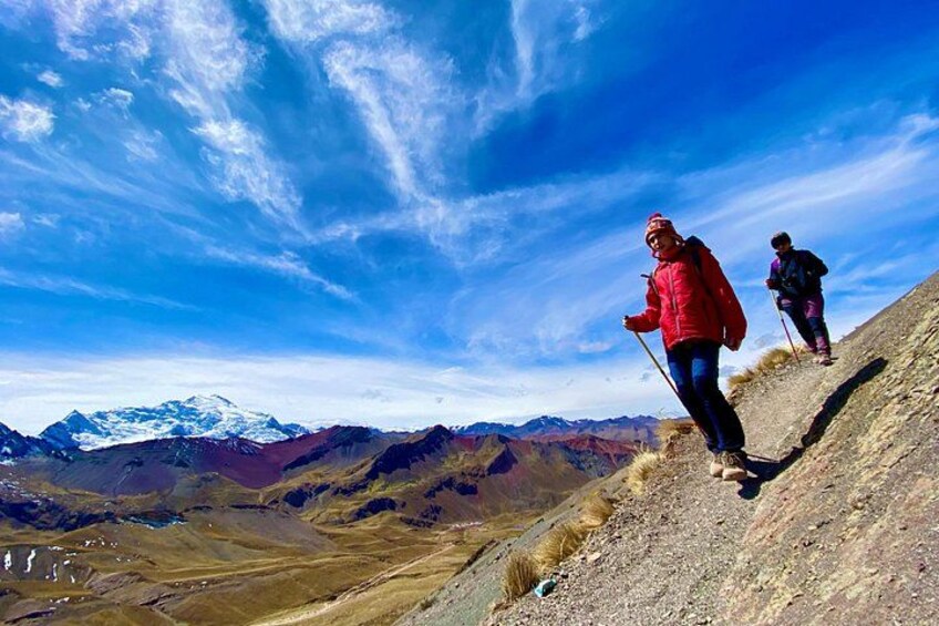 Two hikers on a mountain trail with a clear sky and distant snow-capped peaks. 5
