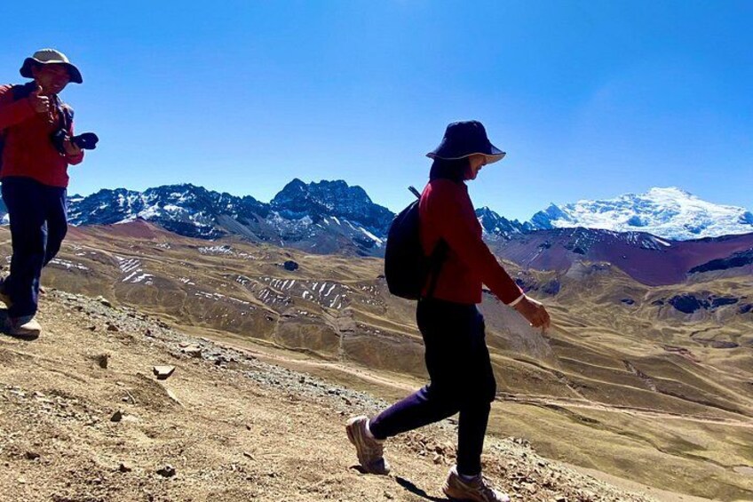 Two hikers on a mountainous terrain with snow-capped peaks in the background. 3