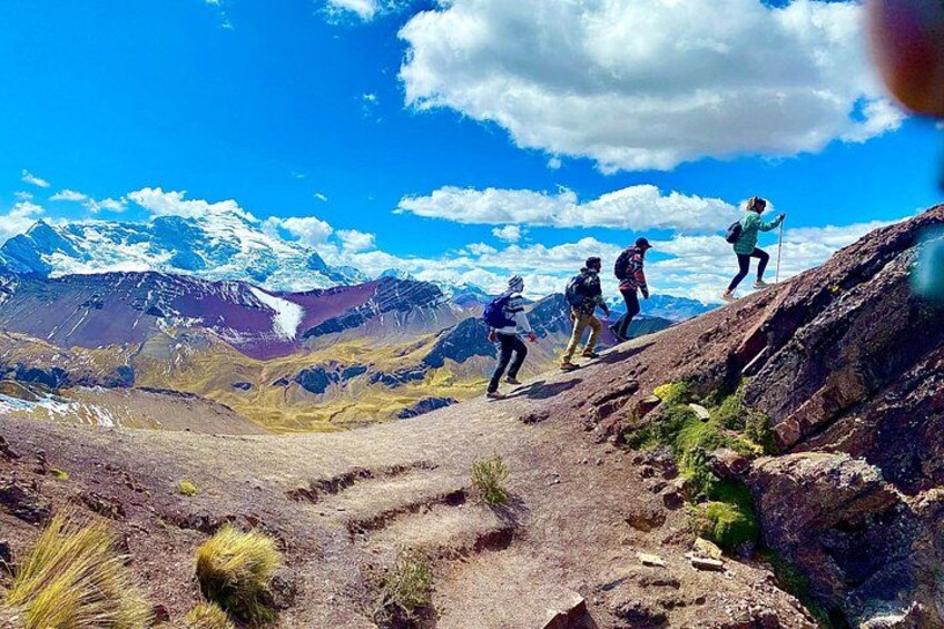 A group of hikers ascending a rocky mountain path with snow-capped peaks in the background. 2