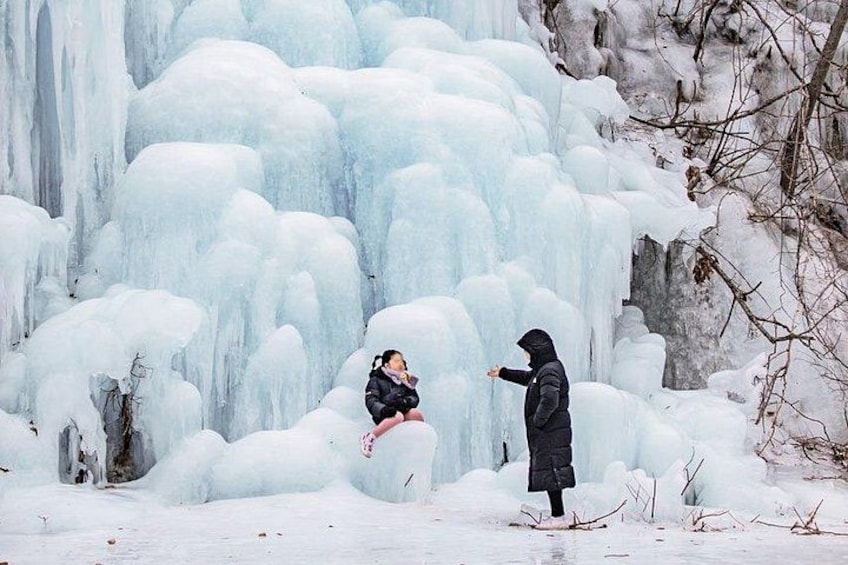 A person taking a photo of a large ice formation with another person in the foreground. 1