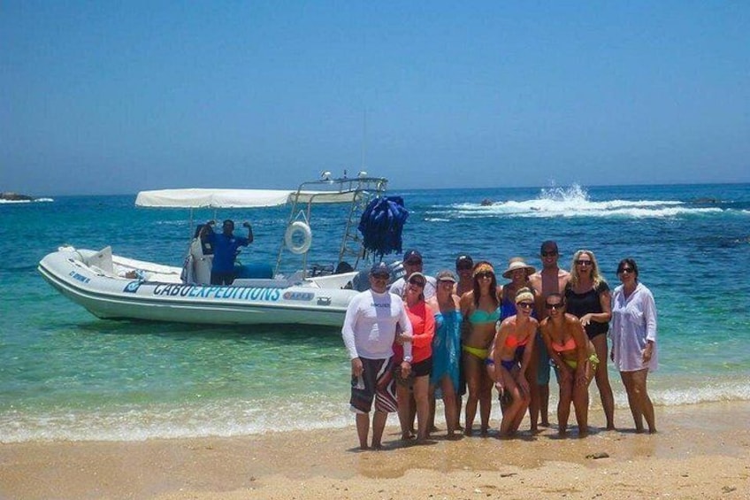 Un grupo de personas en una playa, con un barco identificado como 'CABO EXPEDITIONS' al fondo. 2