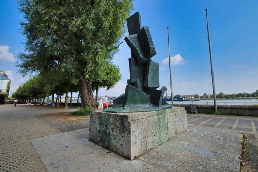 Een sculptuur in een open setting, met een boom en een waterpartij op de achtergrond. 3