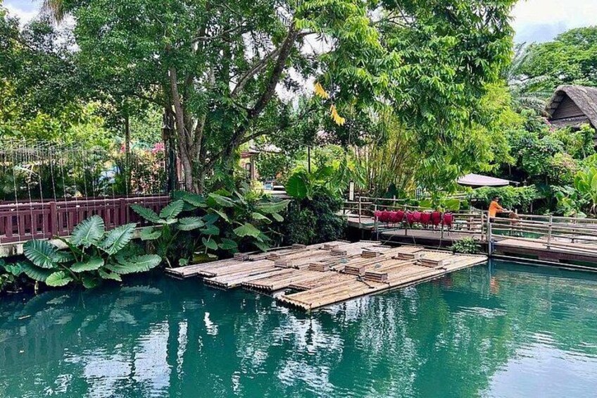 A wooden dock extending into a clear blue pool surrounded by lush greenery and a thatched-roof structure. 5