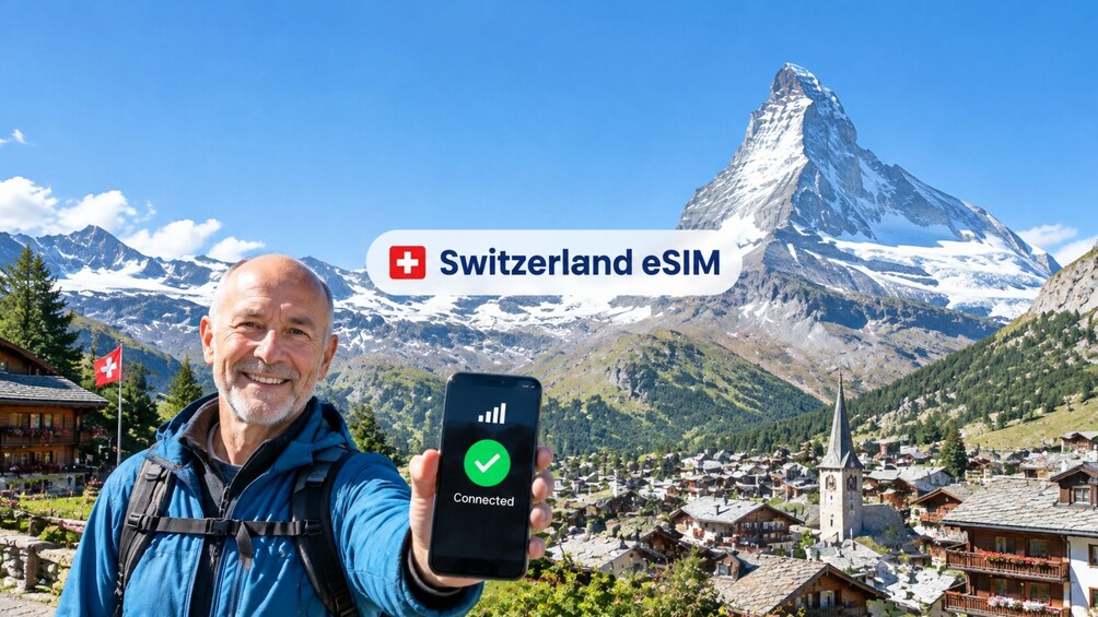 A person holding a smartphone with a connected signal icon, in front of a mountain landscape with a prominent peak and a village below. 1