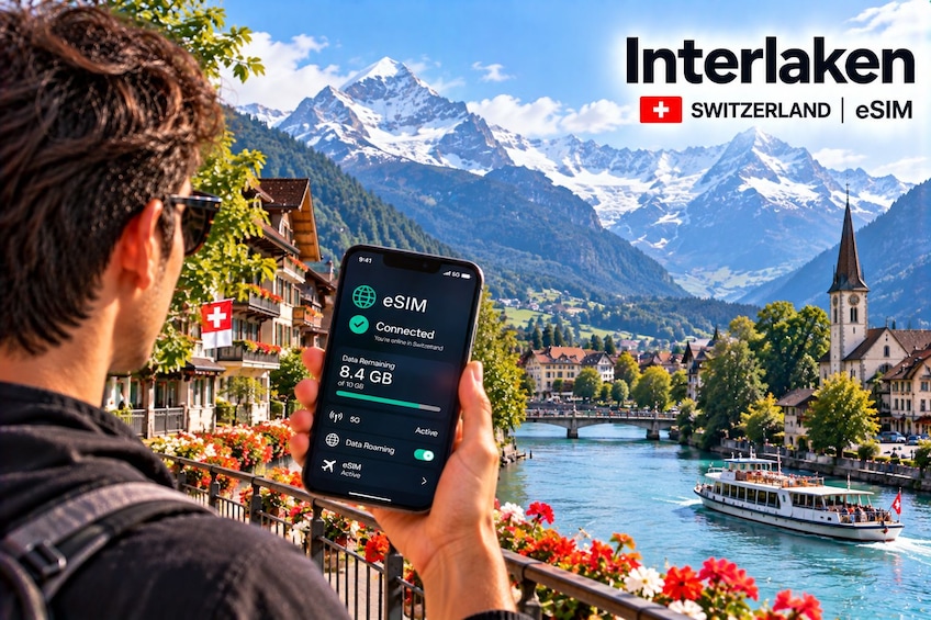 A person holding a smartphone displaying eSIM data usage in a scenic Swiss town with mountains in the background. 5