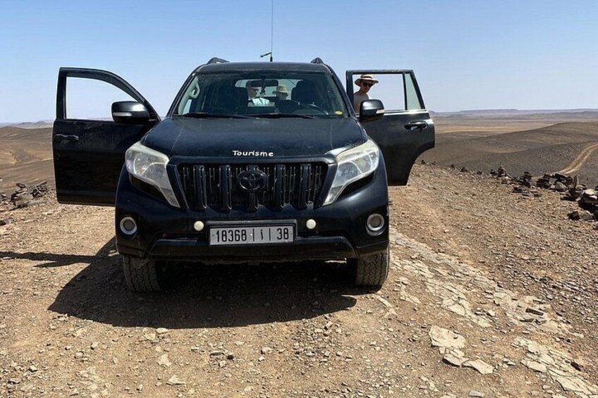 Een zwarte SUV met openstaande deuren, geparkeerd op rotsachtig terrein met een heldere lucht op de achtergrond. 3