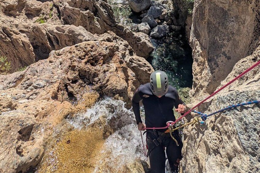 Una persona haciendo rappel por un risco rocoso, con casco y arnés. 3