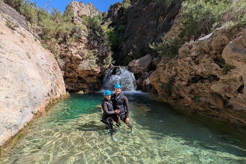 Dos personas con polainas cerca de un cuerpo de agua clara con una cascada en un cañón rocoso. 2