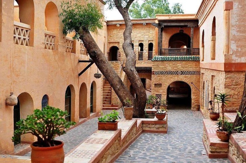 Ein architektonischer Innenhof mit Bögen, Kübelpflanzen und einem Baum. 1