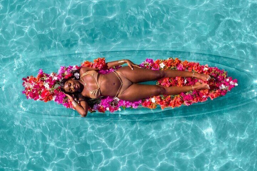 Une personne allongée sur une plateforme flottante dans une piscine, entourée de fleurs aux couleurs vives. 3