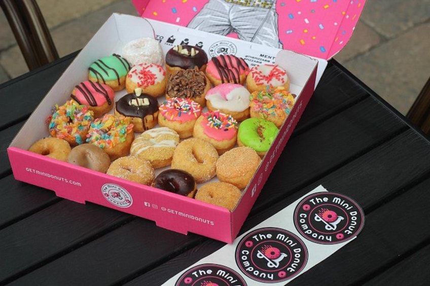A pink box of assorted donuts on a black table with a logo sticker. 2