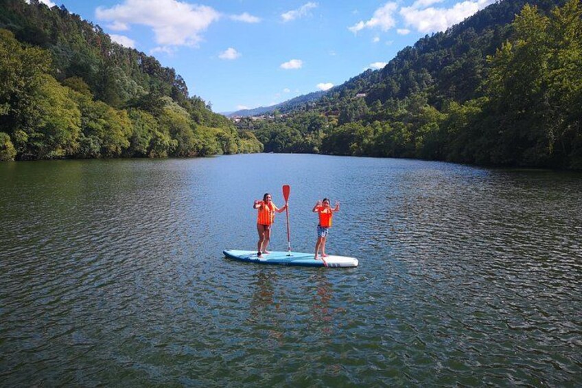 Two people paddleboarding on a calm lake surrounded by lush green hills. 2