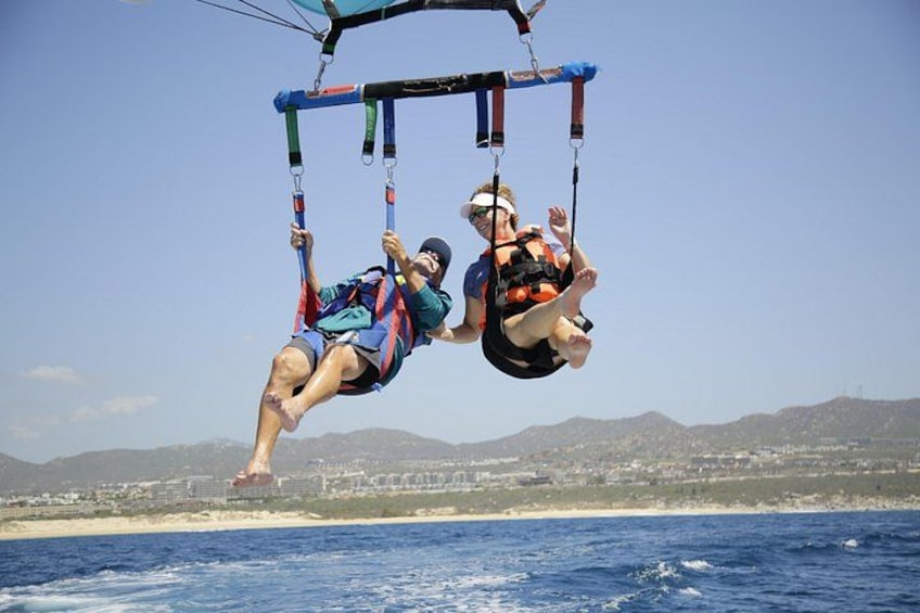 Dos personas practicando parapente sobre una zona costera, con montañas al fondo. 2