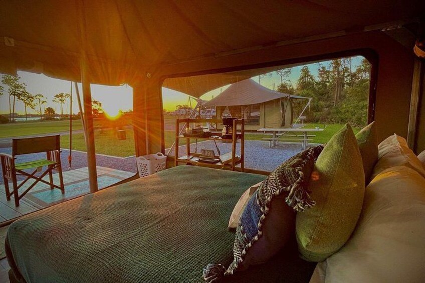 A tented accommodation with a bed, pillows, and a view of the sunset. 4