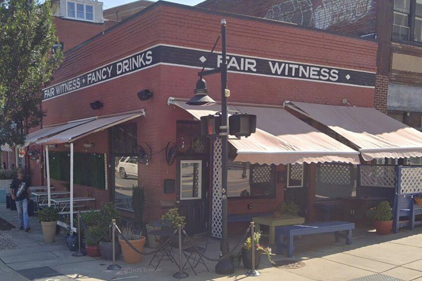 A brick building with awnings labeled 'Fair Witness Fancy Drinks.' 2