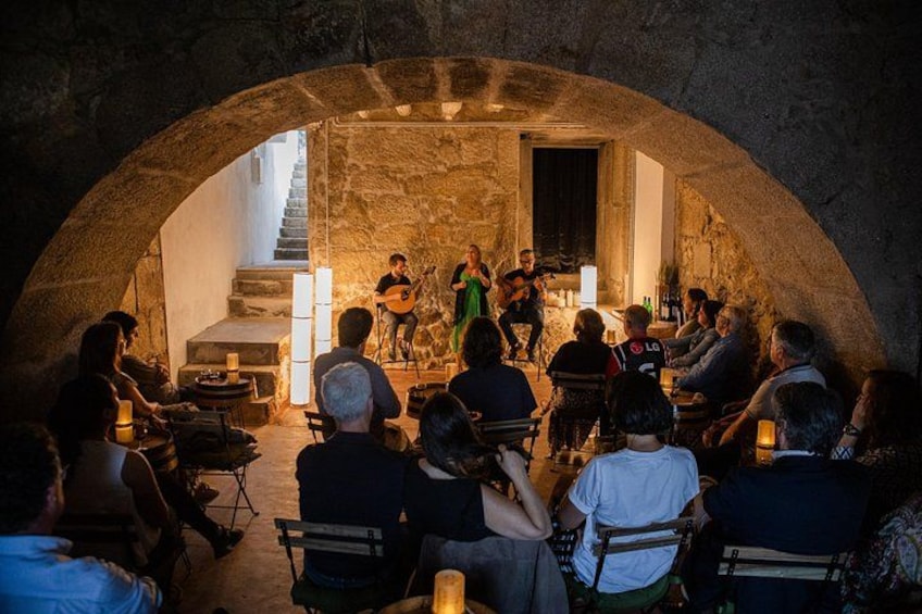 A group of people seated in a stone-walled room, watching a musician perform on a stage. 5