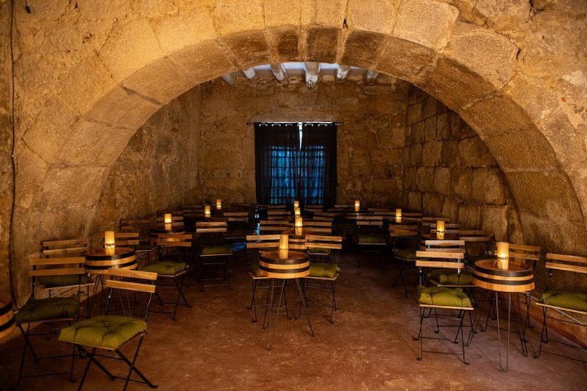 A stone-walled room with round tables and chairs, a window with blue curtains, and candles on each table. 2