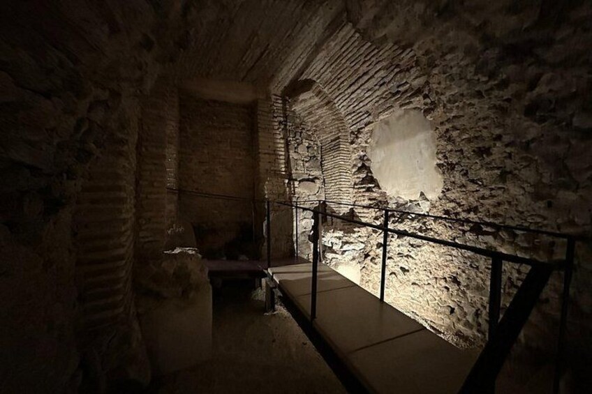 Une chambre souterraine faiblement éclairée, aux murs de pierre et dotée d’une rambarde en métal. 2