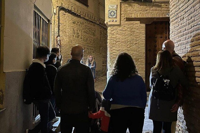 Un gruppo di persone in un vicolo stretto, con pareti in mattoni e una porta di legno. 4