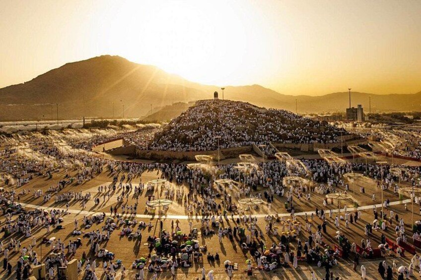 A large gathering of people in a desert setting with a prominent hill in the center. 4