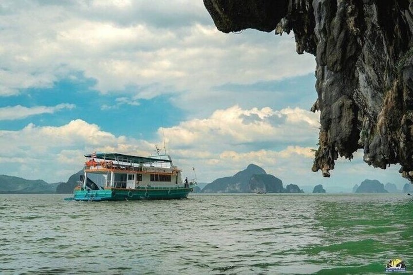 A boat on calm water with a rocky cliff in the foreground and distant islands in the background. 2