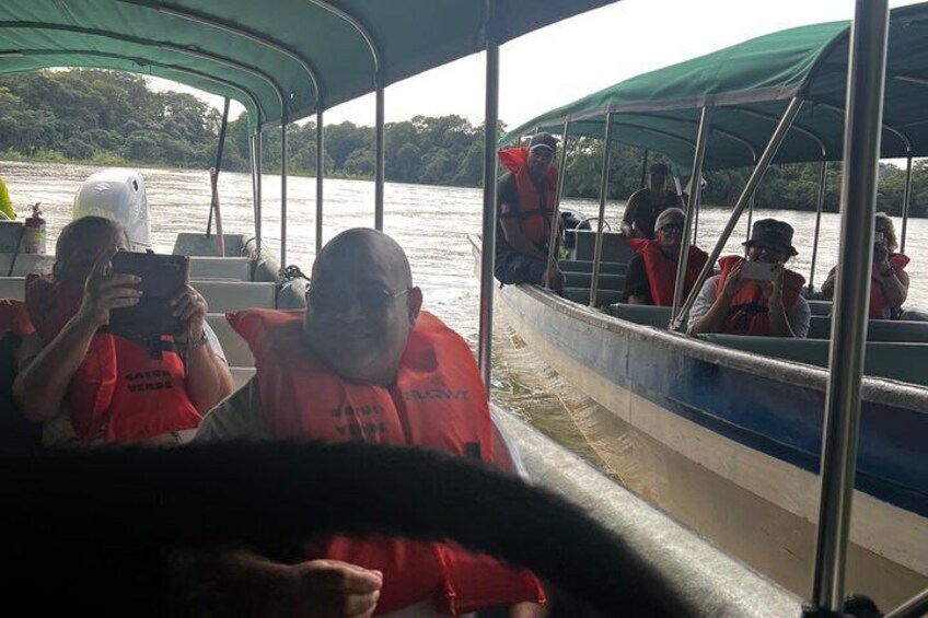 A boat with passengers wearing life jackets, a river, and greenery in the background. 4