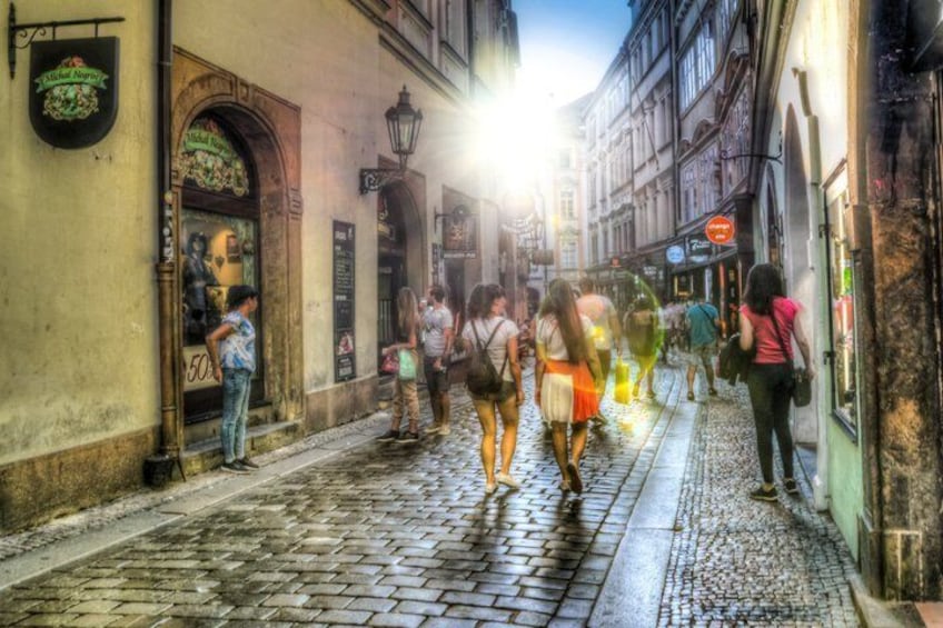 A cobblestone street with pedestrians, historic buildings, and a brightly lit shop. 3