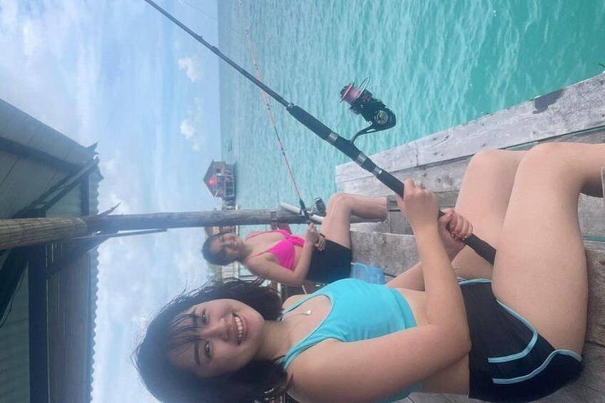 Two individuals fishing by a dock with a body of water in the background. 4