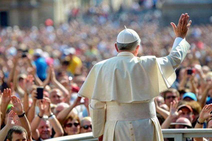 A crowd of people with a person in a white robe and a white hat standing with arms raised. 1