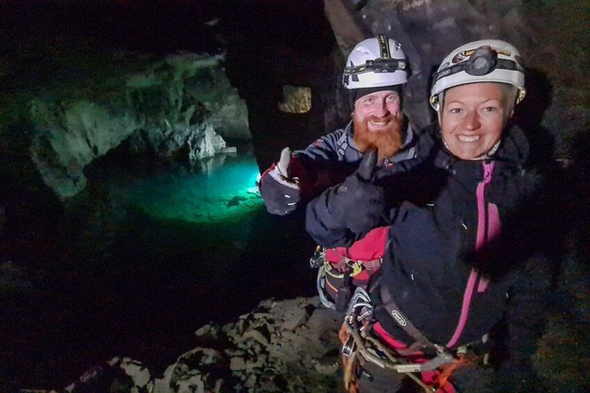 Two people in helmets and climbing gear in a cave with a green light. 3