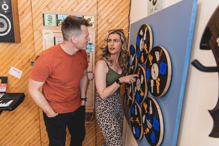 A man and a woman in a room with wooden walls, a blue panel with clocks, and a keyboard on a stand. 3