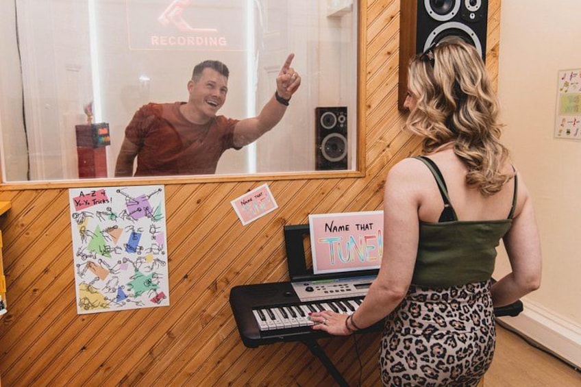 A person standing in front of a keyboard with a sign that reads 'Name That Tune.' 2