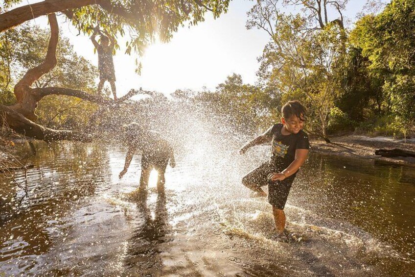 A person splashing water in a natural setting with trees and a body of water. 1