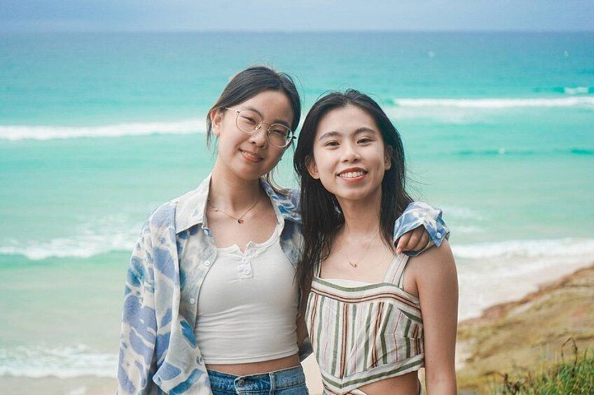 Two people standing on a beach with ocean waves in the background. 1
