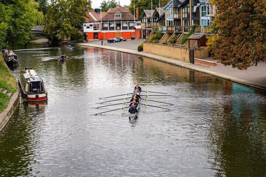 A rowboat with paddles on a canal, a narrowboat, and houses along the canal. 4