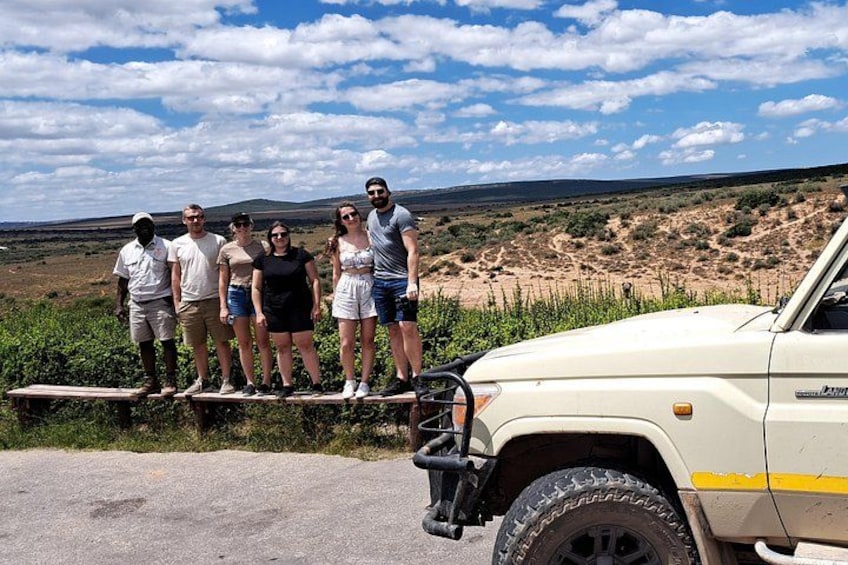 A group of people standing on a ledge next to a vehicle in a desert landscape. 5