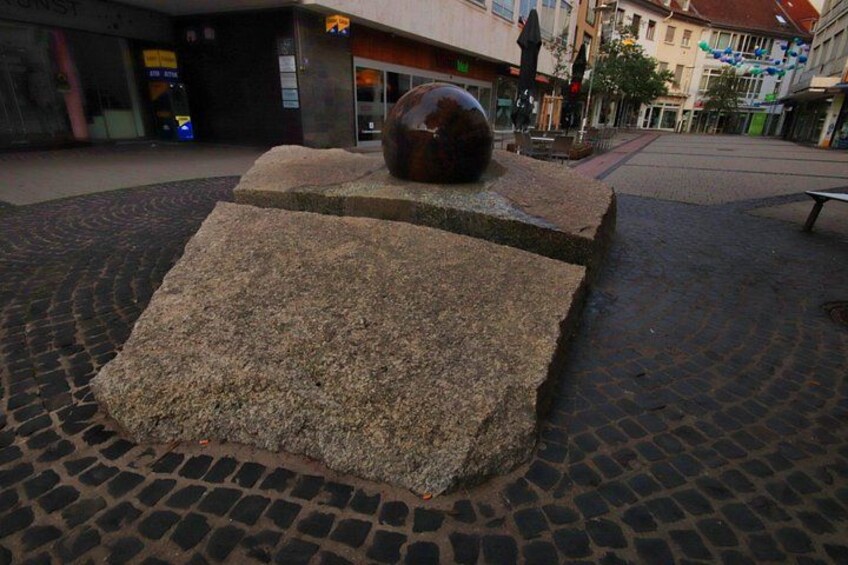 A cobblestone plaza with a large spherical sculpture and a bench. 3