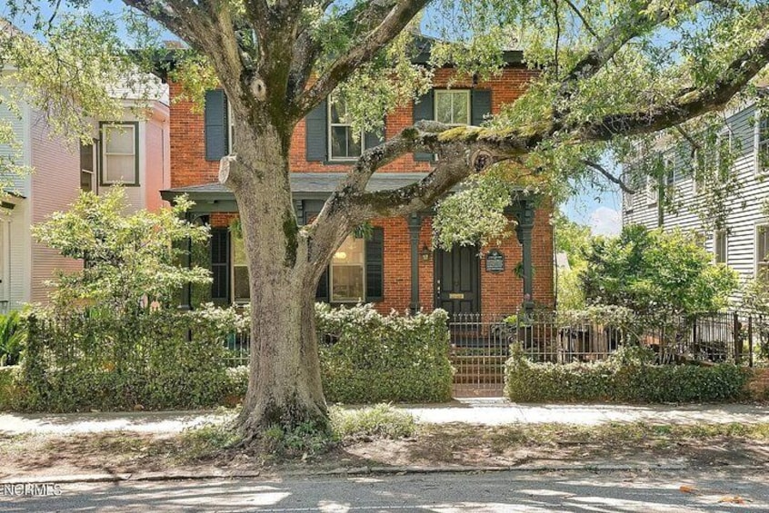 Une rue résidentielle bordée d’arbres, avec une maison en briques, un trottoir et une clôture en métal. 2